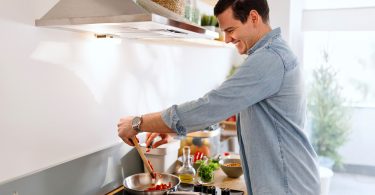 Um homem cozinhando enquanto a coifa funciona. Coifa depurador.