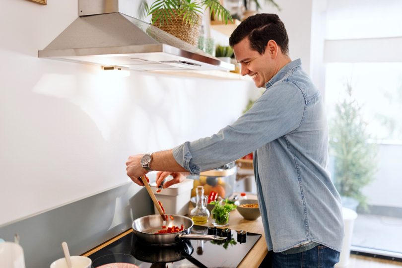 Um homem cozinhando enquanto a coifa funciona. Coifa depurador.