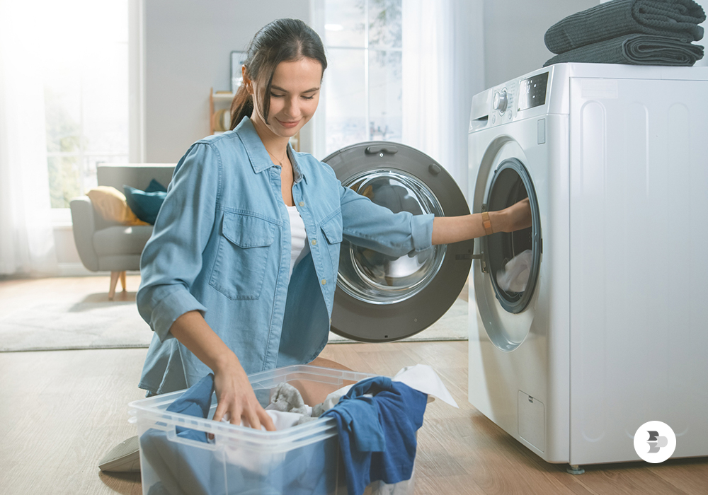 Moça colocando as roupas sujas na máquina de lavar. Máquina de lavar ideal.