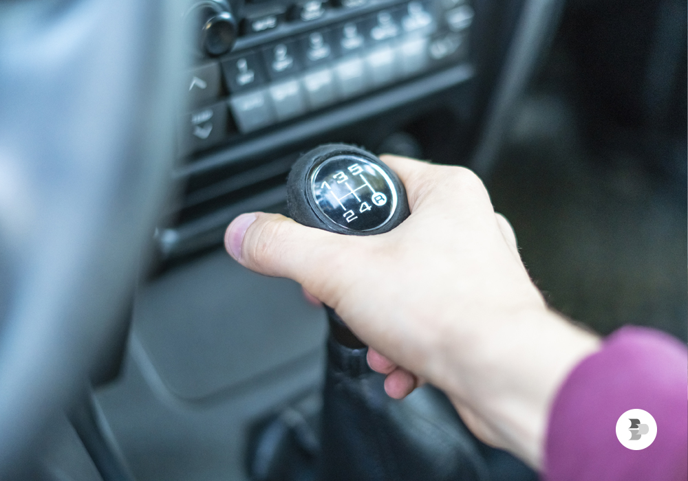 Uma pessoa deixando a mão na alavanca de marchas do carro. Hábitos volante.