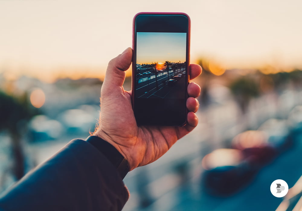 Uma pessoa fotografando o pôr-do-sol em um estacionamento. Dicas fotografia.