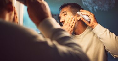 friendly man cuts his own hair with a machine in front of the mirror picture id1303368071