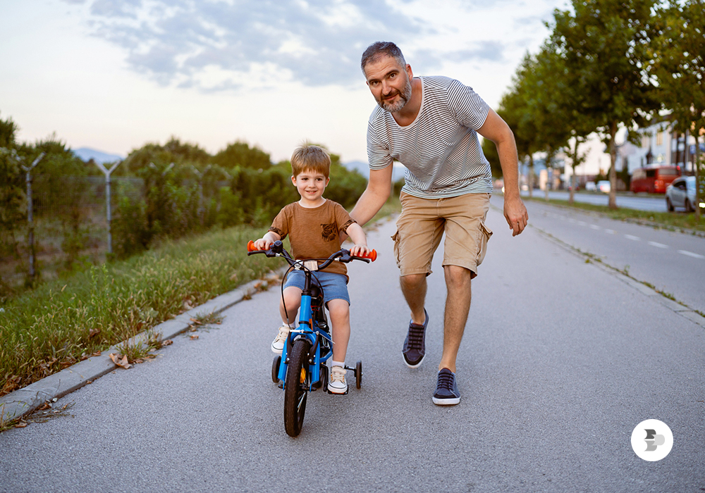 Um pai ajudando o sue filho a pedalar. Bicicleta.