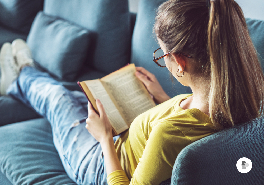 Mulher sentada no sofá lendo um dos melhores livros para ler sobre a vida.