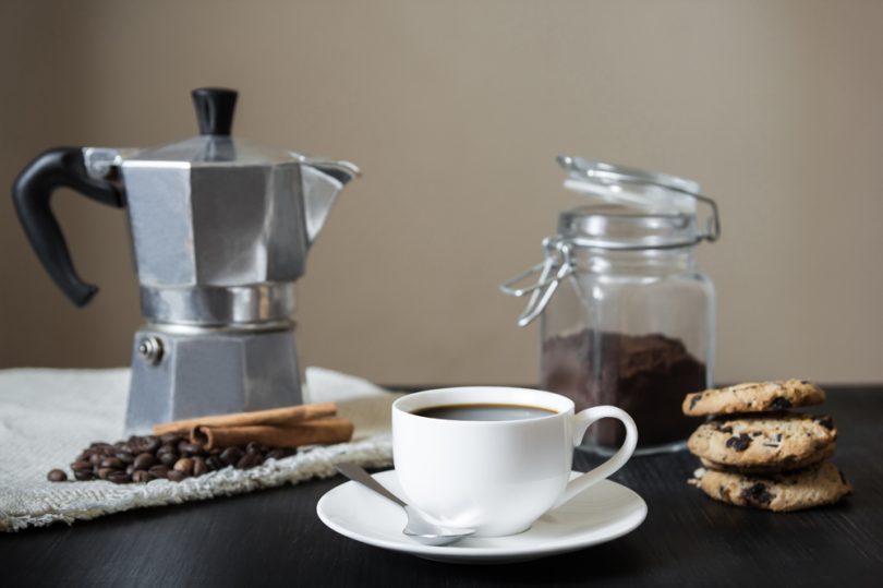 Uma mesa com bule italiano, cookies, grãos de café e café passado. Cantinho do Café.