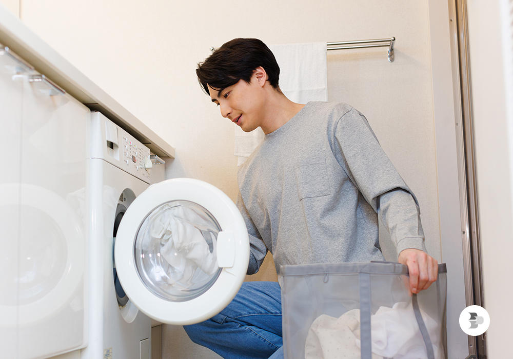 Um homem colocando as roupas na secadora. Secadora de Roupas.