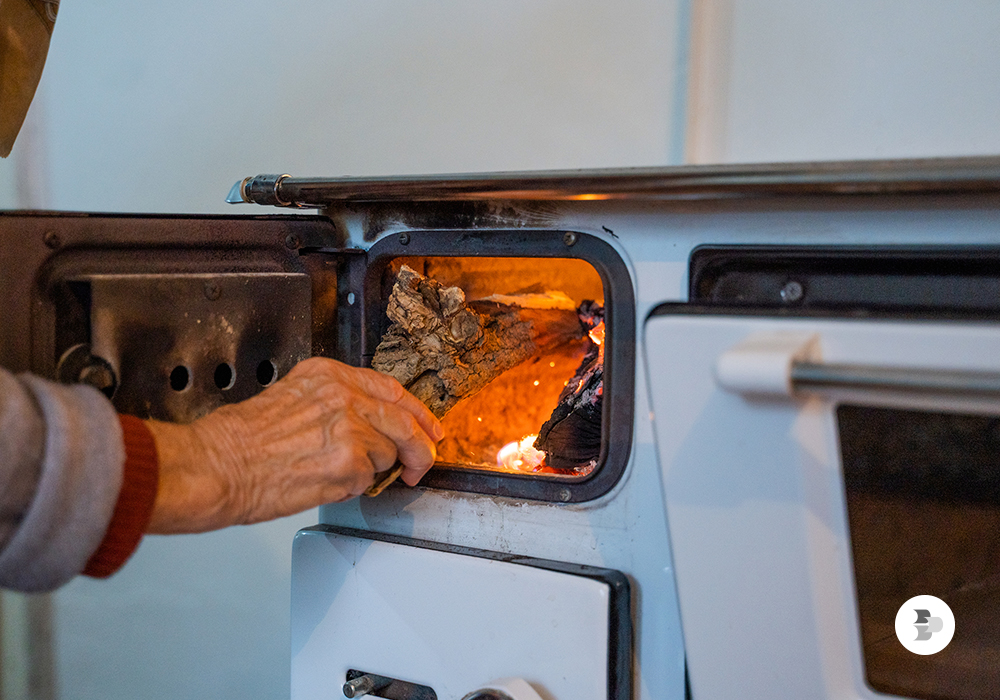 Uma pessoa colocando lenha no fogão, para esquentar a casa. Fogão a lenha.