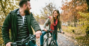 Casal de jovens andando de bicicleta em uma estrada. Black Friday Esporte Lazer.