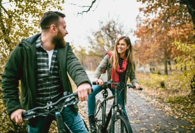 Casal de jovens andando de bicicleta em uma estrada. Black Friday Esporte Lazer.