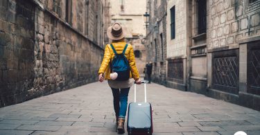 Uma turista passeando com sua mala em uma rua de uma cidade espanhola. Mala Viagem.