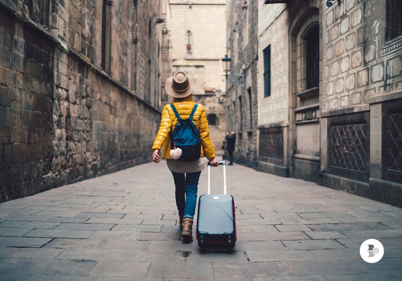 Uma turista passeando com sua mala em uma rua de uma cidade espanhola. Mala Viagem.