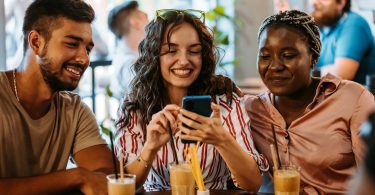 Um trio de jovens usando um smartphone. Black Friday Smartphone Celular.