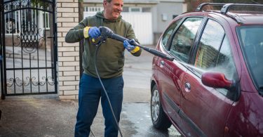 Um homem lavando o seu carro em casa. Lavadora Alta Pressão.
