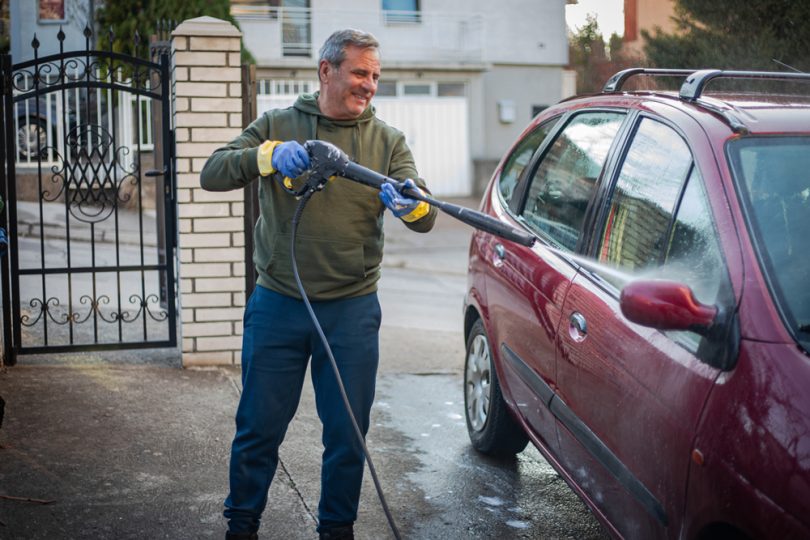Um homem lavando o seu carro em casa. Lavadora Alta Pressão.