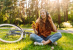 Uma jovem moça sentada na grama ouvindo música, com a bicicleta ao lado. Músicas ouvir.