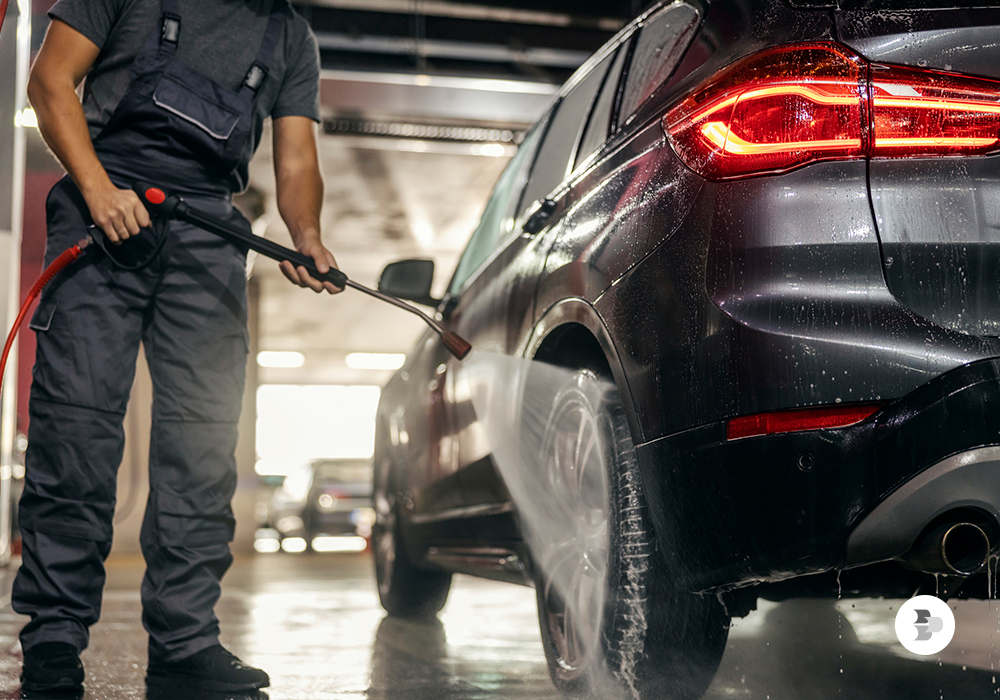 Um homem com a lavadora de alta pressão lavando um carro. Lavadora alta pressão.