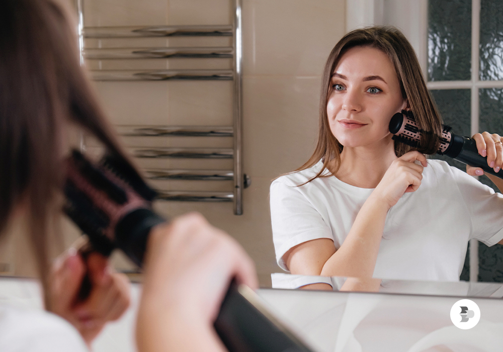Uma mulher secando e penteando seu cabelo com a escova secadora. Escova secadora. 