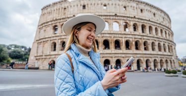 Uma moça em frente ao Coliseu mexendo em seu smartphone. Itália.