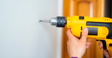 Uma pessoa parafusando a parede. Parafusadeira.