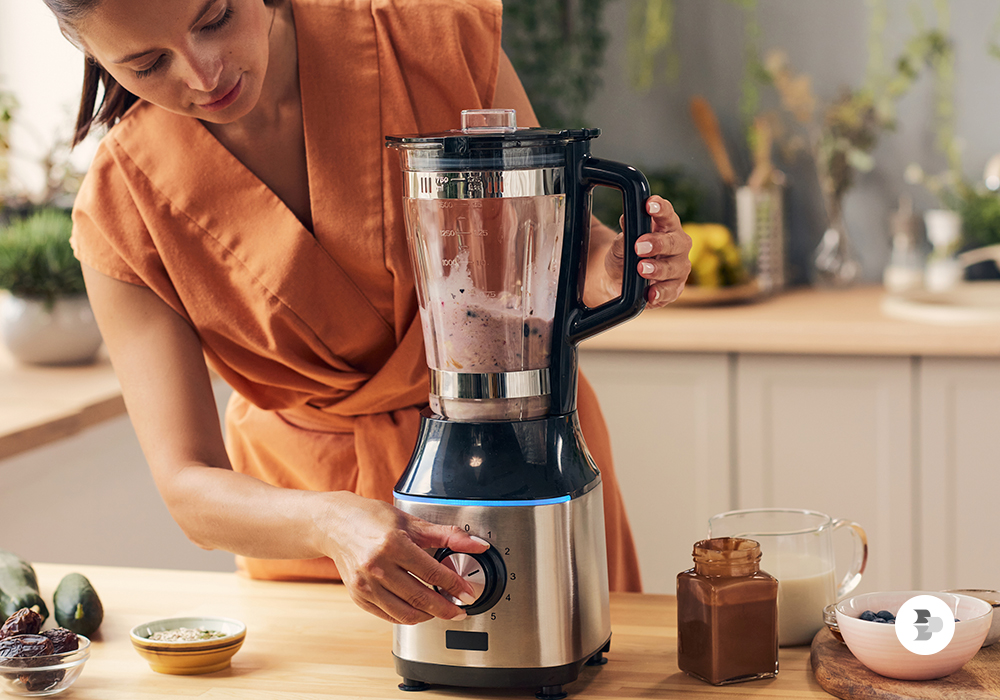 Uma mulher utilizando o liquidificador na cozinha. Liquidificador ideal.