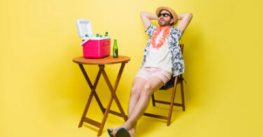 Um homem sentado numa cadeira, com a caixa térmica em cima da mesa. Caixa térmica.