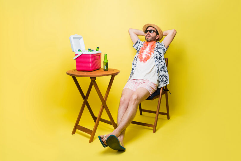 Um homem sentado numa cadeira, com a caixa térmica em cima da mesa. Caixa térmica.