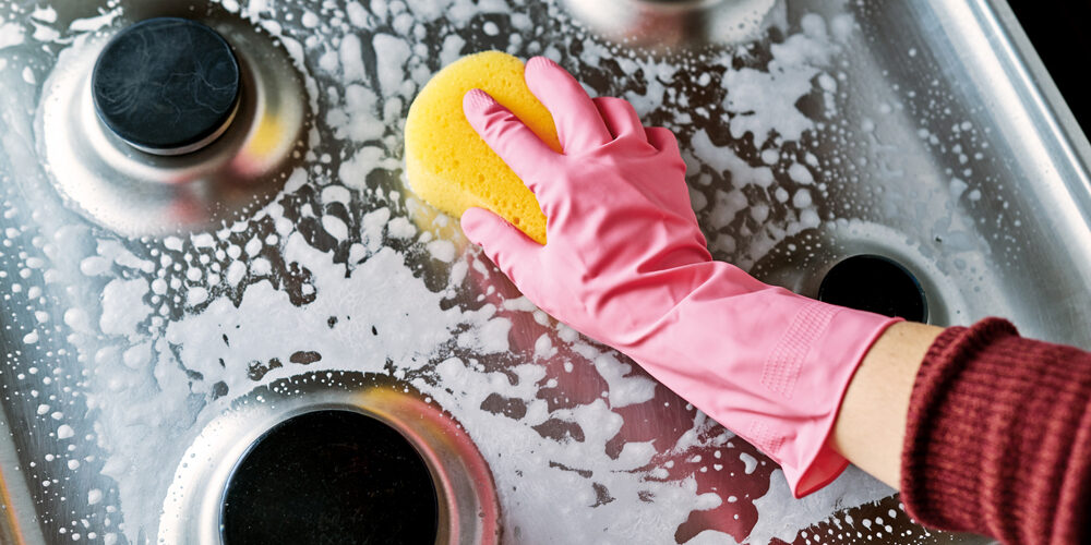 Uma pessoa fazendo a limpeza do seu fogão a gás. Limpar fogão.