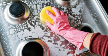 Uma pessoa fazendo a limpeza do seu fogão a gás. Limpar fogão.