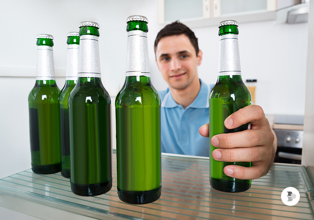 Um homem pegando uma garrafa de cerveja que está dentro da geladeira. Cervejeira.