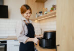 Uma mulher utilizando a air fryer para cozinhar seus aliemntos. Eletroportáteis casa.