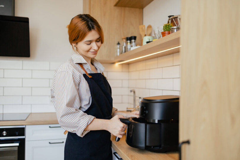 Uma mulher utilizando a air fryer para cozinhar seus aliemntos. Eletroportáteis casa.